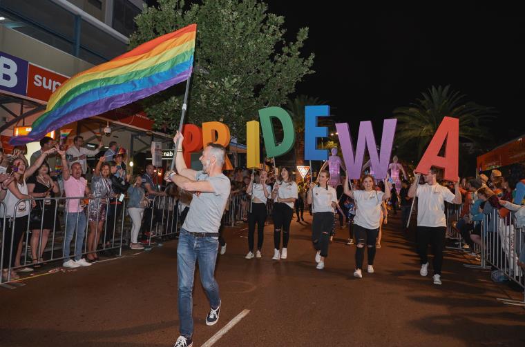People walk down a street holding a rainbow flag and the letters PRIDE WA