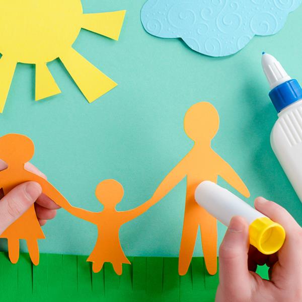 Child's hands creating a paper cut out family scene.