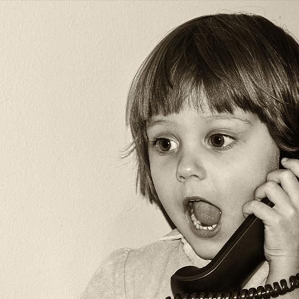 Monochrome image of a young girl on an old-fashioned dial telephone.