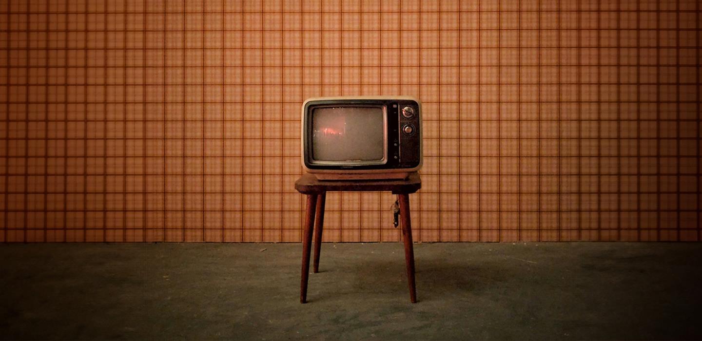 Retro television on stand in bare room with concrete floor and square orange wallpaper background.