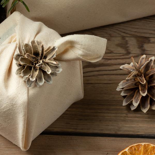 Present wrapped in natural material, decorated with pine cones and dried orange slices.
