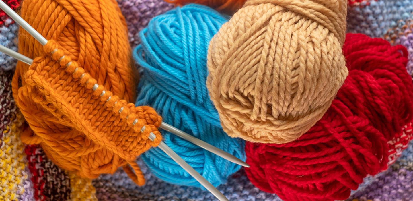 Orange wool on knitting needles surrounded by coloured balls of wool.