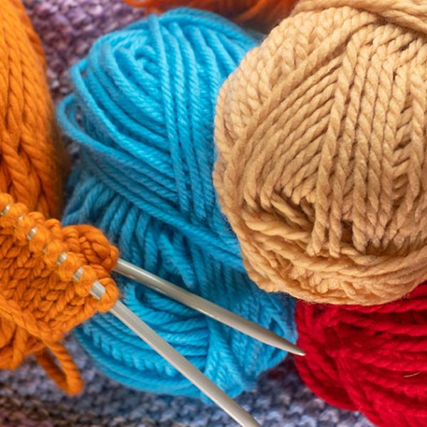 Orange wool on knitting needles surrounded by coloured balls of wool.