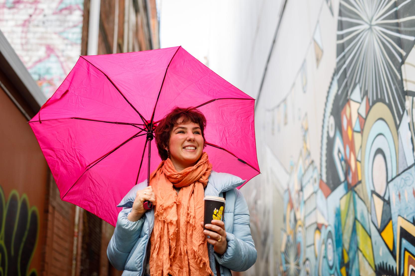 Girl holds umbrella in art filled laneway