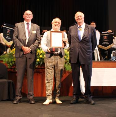 Tibor Meszaros holding a certificate and standing in between Cmr Andrew Hammond and Kim Beazley.