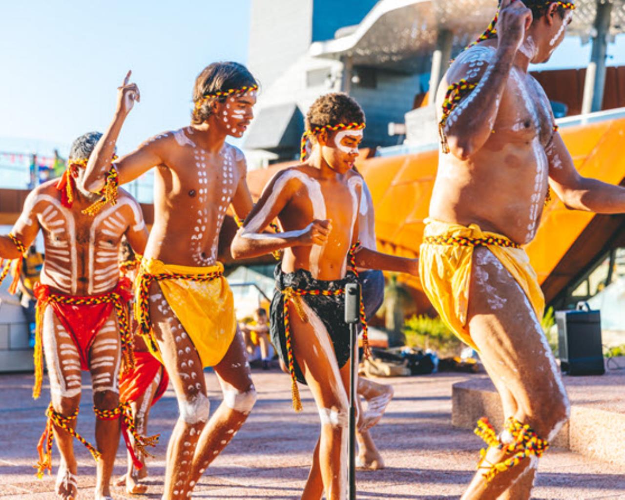 Aboriginal children and adults dance wearing coloured outfits