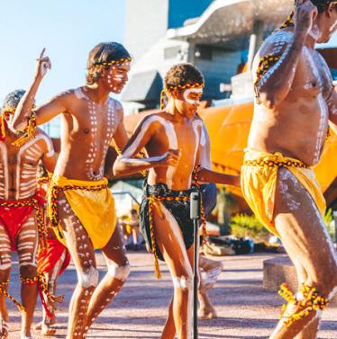 Aboriginal children and adults dance wearing coloured outfits
