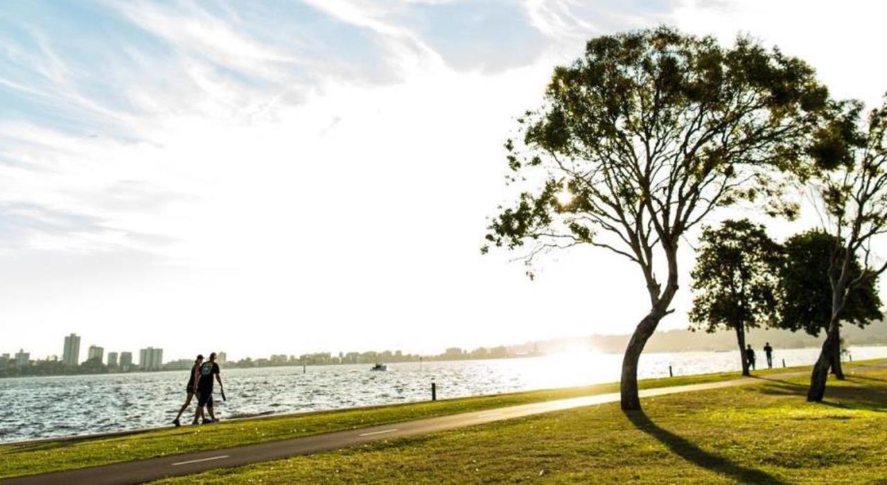 Swan River Foreshore with walkers along the footpath and the sun shining, and some green trees