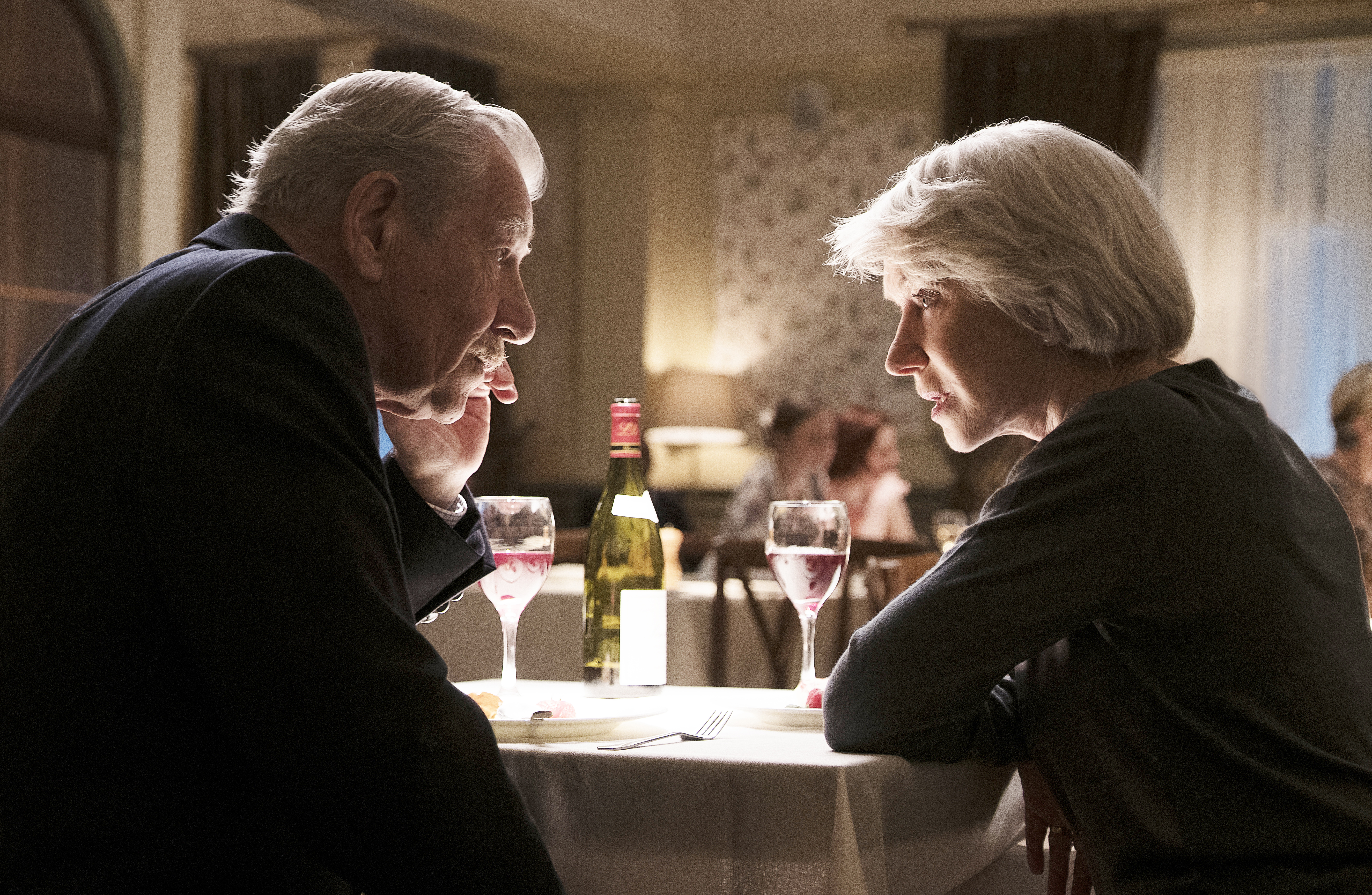 Movie still from The Good Liar with Dame Helen Mirren and Sir Ian McKellen whispering across a table