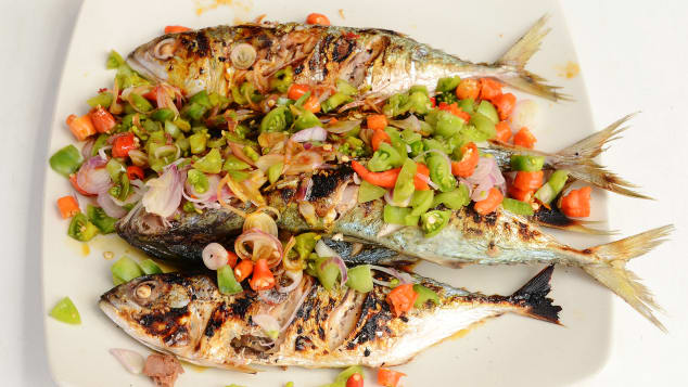 Platter with four cooked, whole fish covered in red and green vegetables 