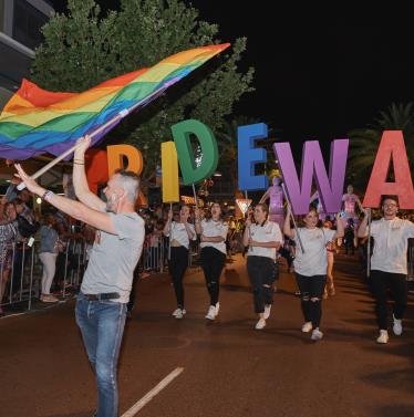 Man holding rainbow flag in parade in front of PRIDE WA letters