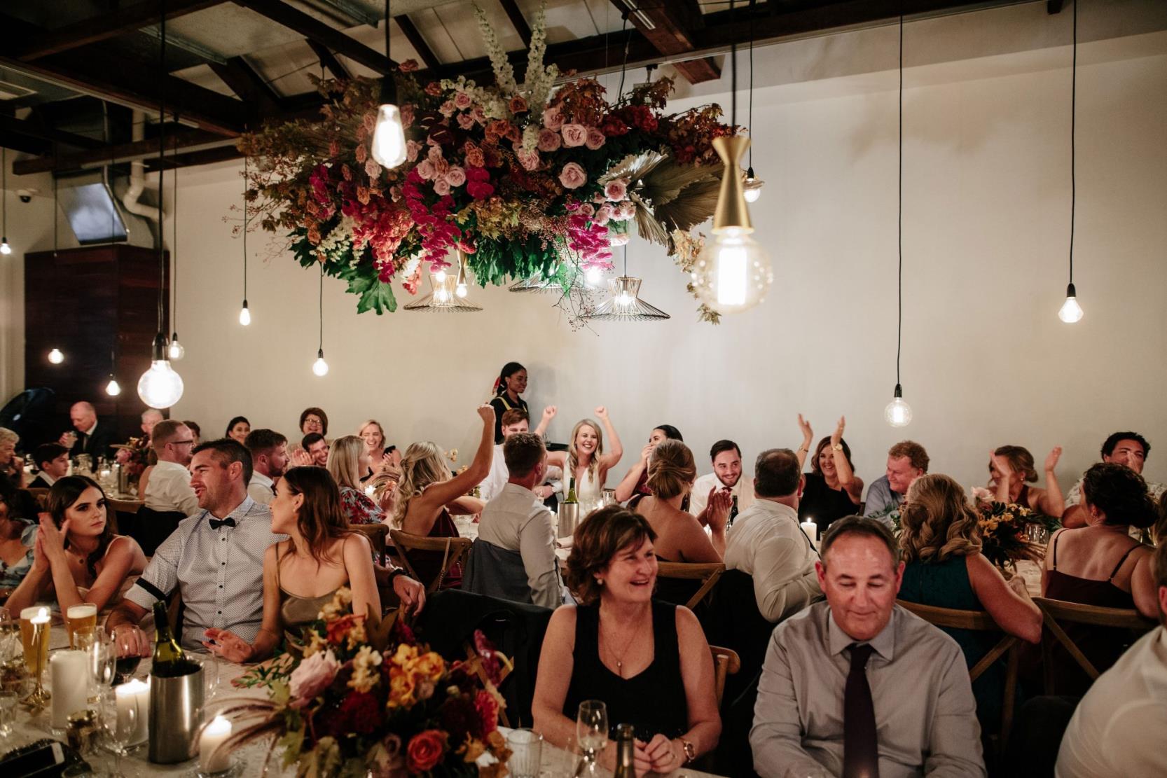 Wedding guests at table with floral centerpiece hanging from roof