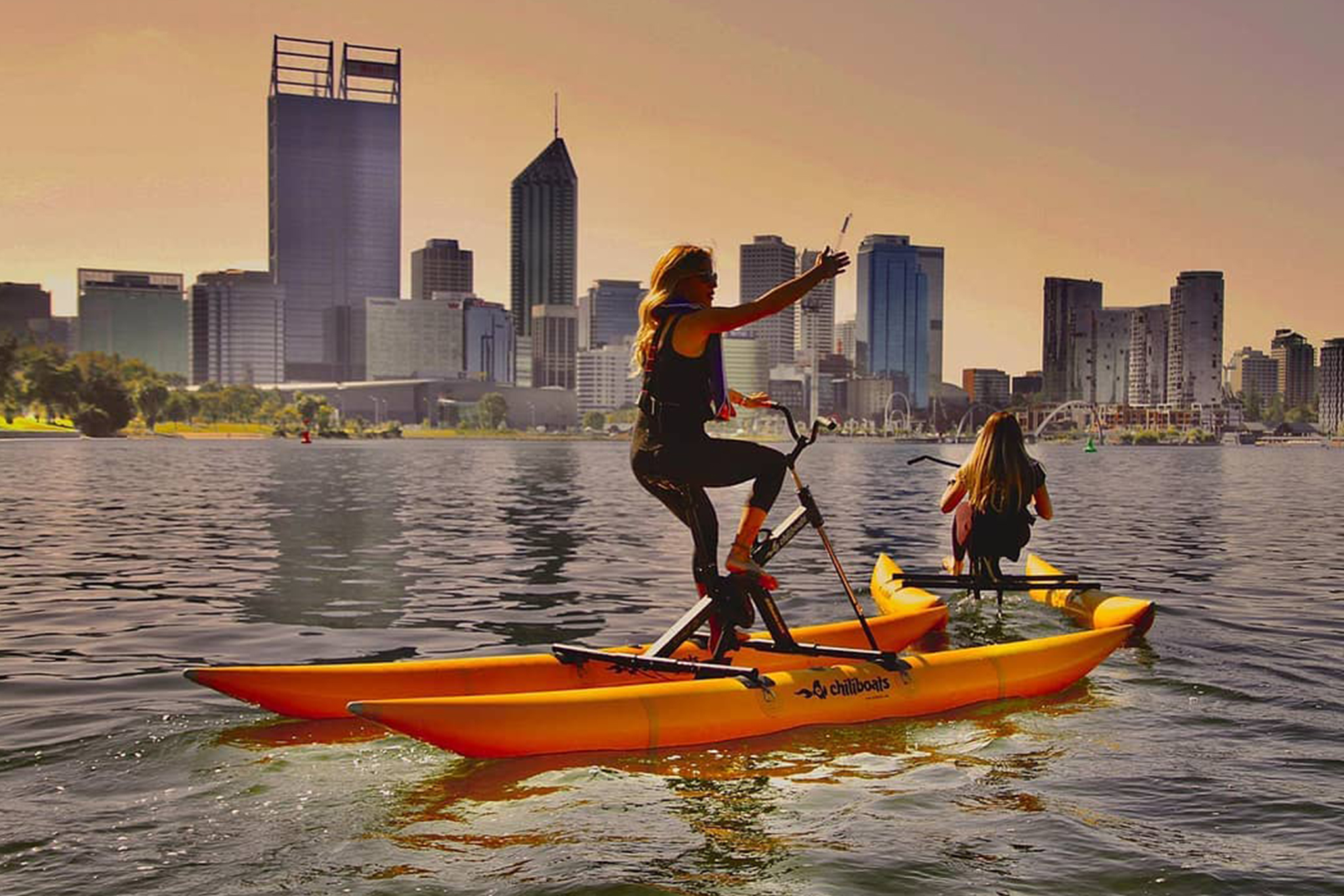 Two people riding water bikes on Swan River facing the city