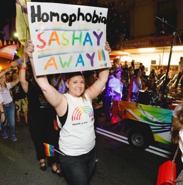 Person walking in Pride Parade holding sign that says "Homophobia Sashay Away!"