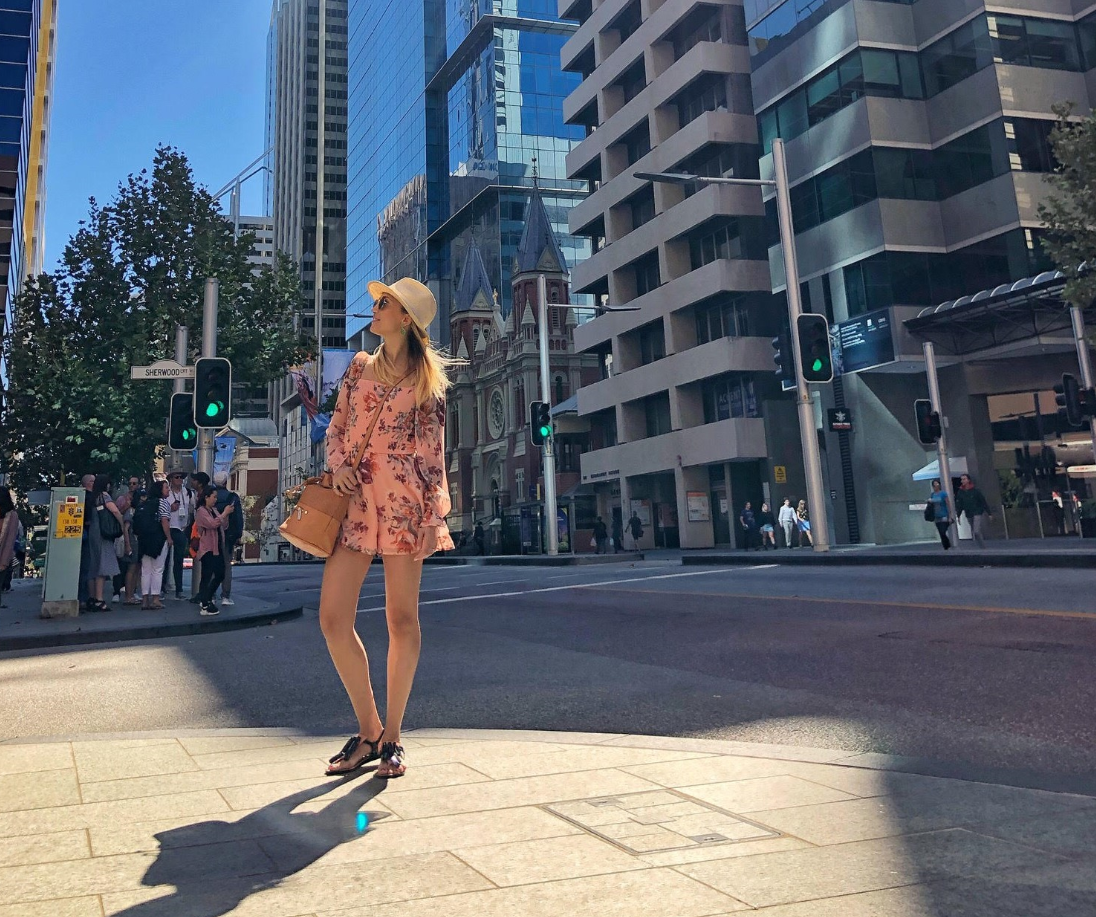 Lady standing on the sidewalk with city buildings behind her